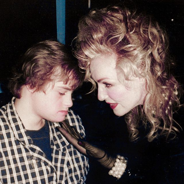 Julie Newmar in a black dress caressing her son John Jewl Smith wearing a check shirt.